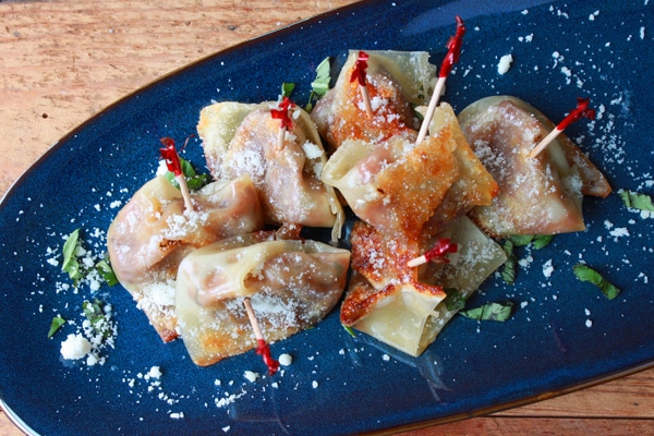 Pumpkin wontons on a blue serving plate sprinkled with parmesan cheese